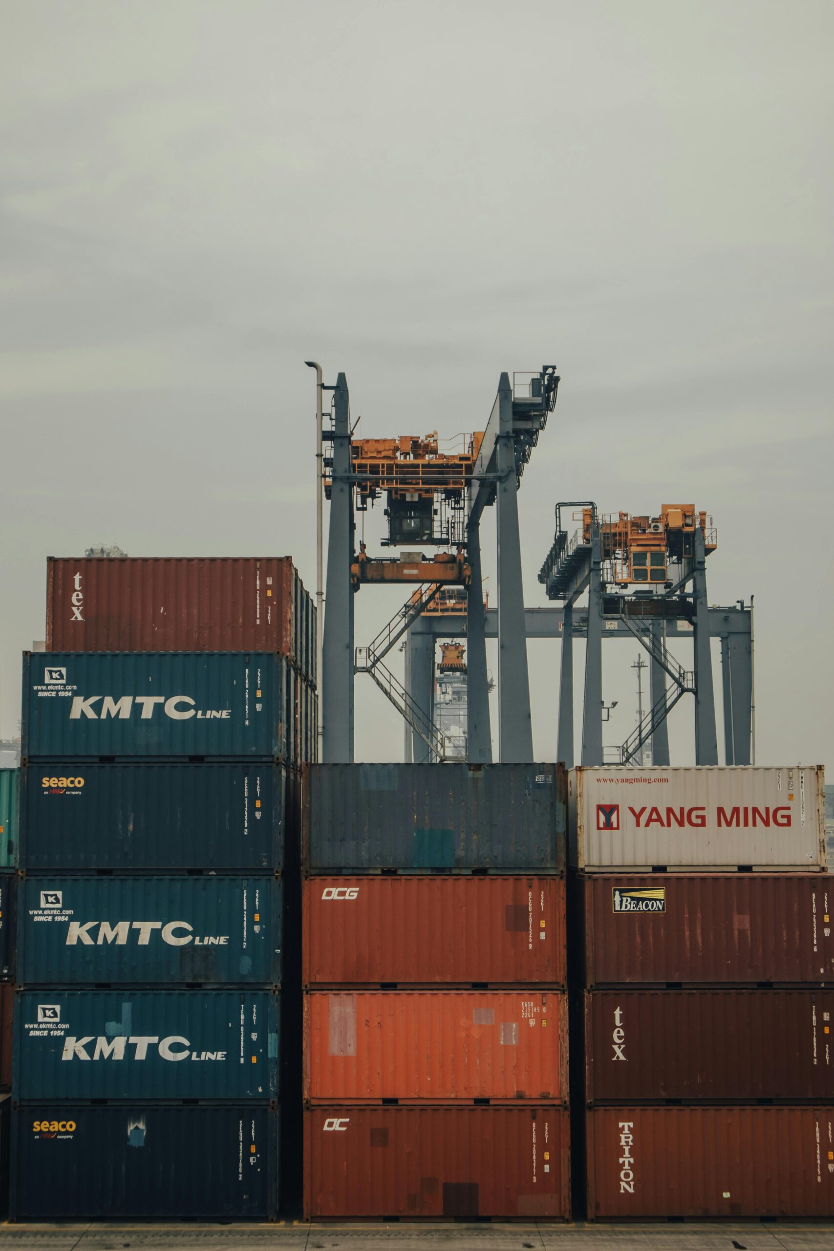 Stacked shipping containers with cranes at Jakarta port reflect global logistics operations.